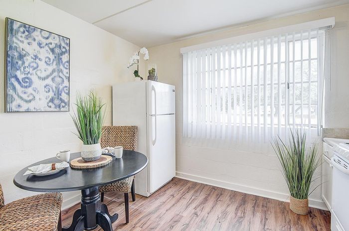 Bright and inviting kitchenette with a round table, stylish woven chairs, modern artwork, and a large window with blinds.