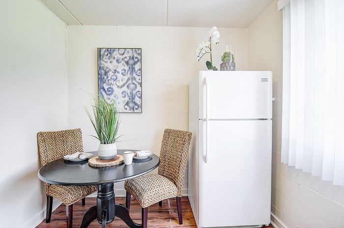 Charming dining nook with stylish wicker chairs, a round table set for two, elegant white fridge, and modern decor accents.