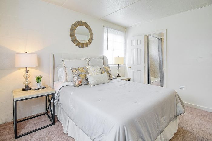 Bright and inviting bedroom with a modern touch, featuring plush white bedding, chic decorative pillows, and elegant bedside lamps.