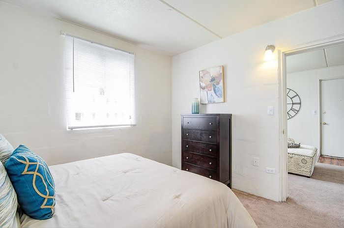 Bright and cozy bedroom with elegant decor, featuring a plush bed, natural light pouring through a window, and a dark wood dresser adding a touch of sophistication.