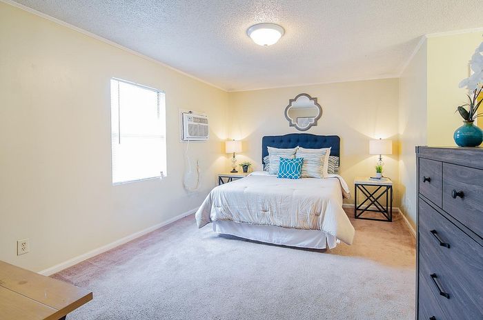 Inviting bedroom with plush carpet, a cozy bed adorned with elegant pillows, and stylish decor creating a warm ambiance.