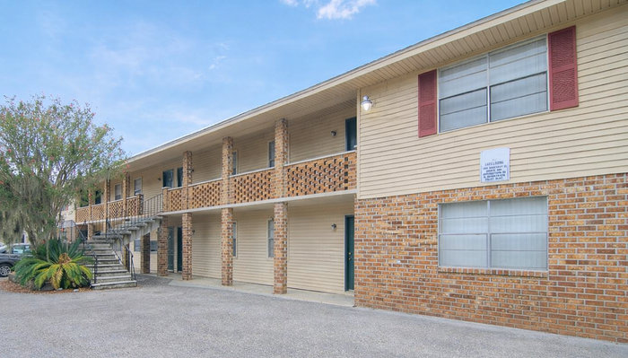 Charming two-story apartment complex with brick facade and lush greenery, offering spacious living in a serene setting.