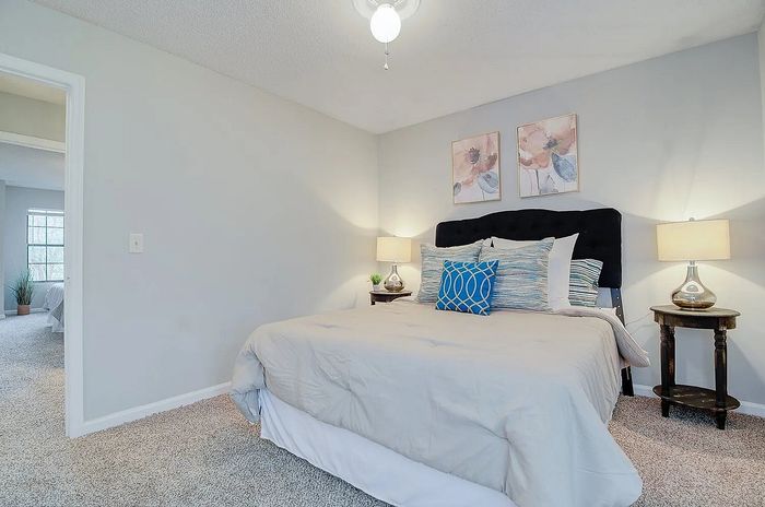 Inviting bedroom with plush carpet, cozy bed accented with colorful pillows, stylish bedside lamps, and modern floral artwork.