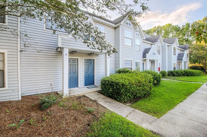 Charming multi-unit townhouse with attractive blue doors, nestled in lush greenery and vibrant landscaping.