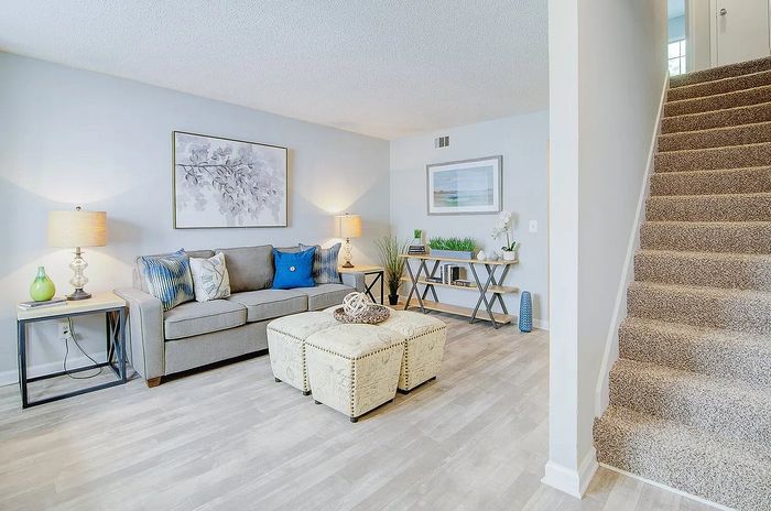 Inviting living room with modern decor, cozy gray sofa, elegant artwork, and plush carpeted stairs offering a warm and stylish ambiance.
