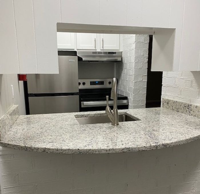 Elegant kitchen pass-through with sleek granite countertop, modern stainless steel appliances, and bright cabinetry.