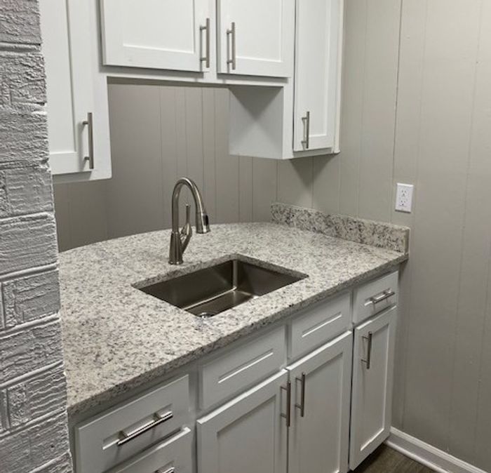 Sleek kitchen corner featuring elegant white cabinets, modern granite countertops, and a polished stainless steel sink, offering a compact yet stylish culinary space.