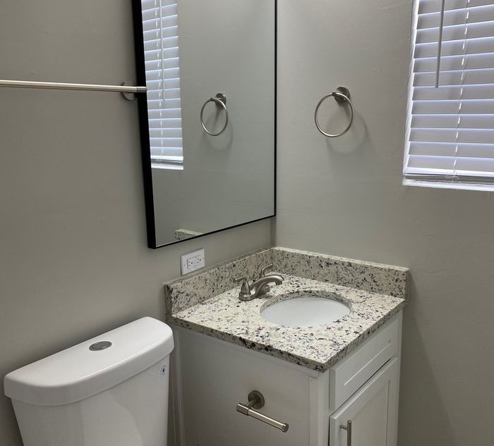Modern bathroom with elegant granite countertop, sleek fixtures, and a large mirror designed for a contemporary appeal.