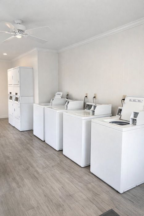 Modern laundry room with multiple washing machines and dryers, featuring sleek white design and ample natural lighting.