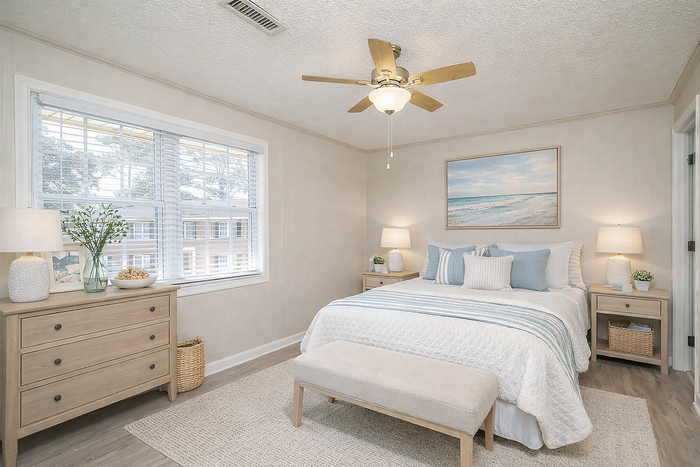 Bright and airy bedroom featuring a cozy bed with a serene ocean-themed decor, large window for natural light, and elegant wooden furniture.