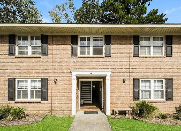 Charming brick apartment building with classic window shutters, surrounded by lush greenery and a welcoming entrance.