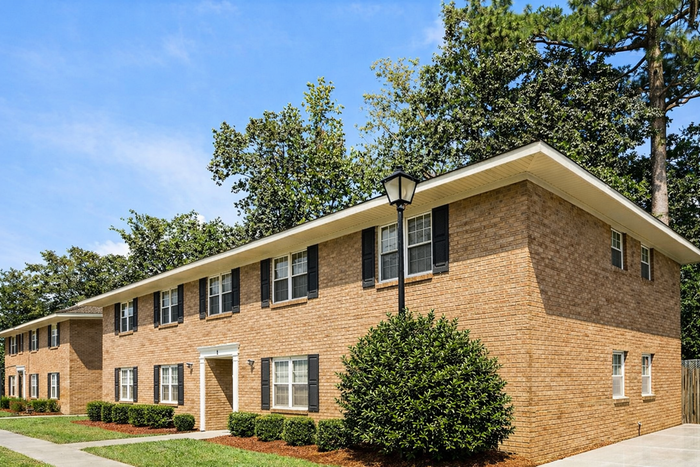 Charming brick apartment building with manicured greenery, offering a serene living environment surrounded by lush trees.