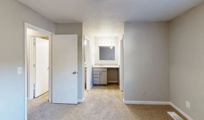 Bright and inviting space with plush carpet, modern vanity area with ample storage, and fresh, neutral walls.