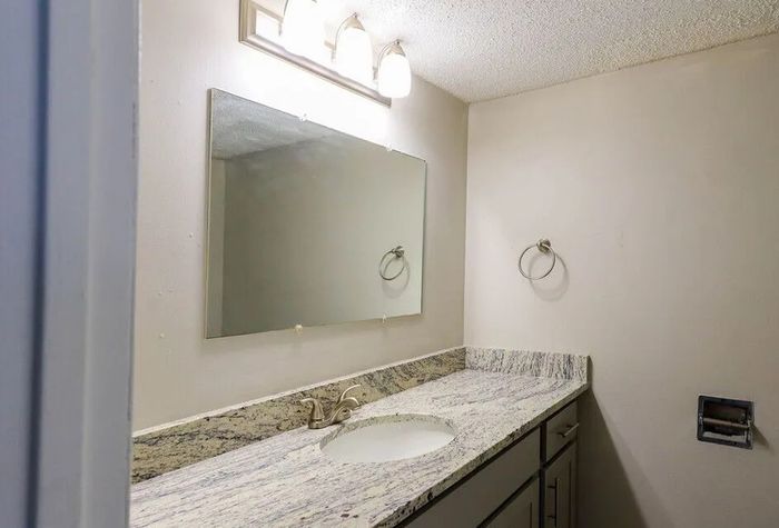 Elegant bathroom featuring a sleek granite countertop, large mirror, and modern light fixtures offering a serene ambiance.