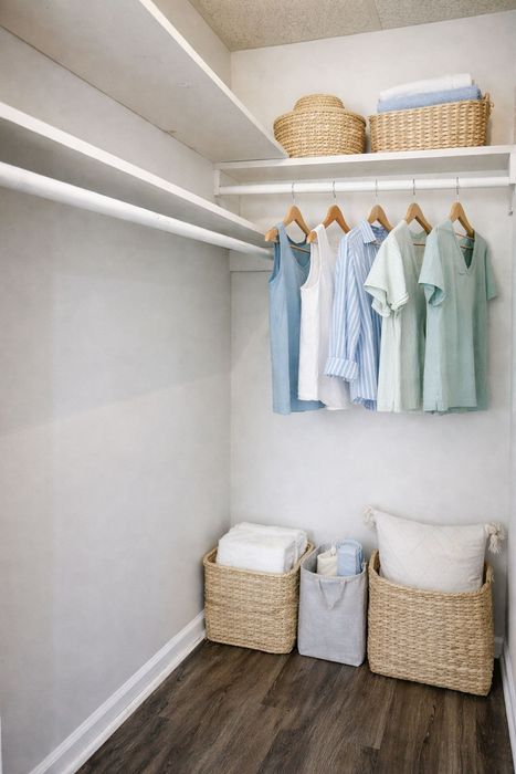 Chic and organized walk-in closet with stylish shelving, hanging clothes in pastel hues, and neat woven baskets on a rich wood floor.