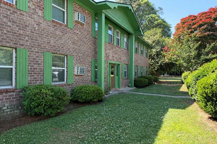 Charming brick apartment building with vibrant green accents, surrounded by lush greenery and colorful trees.