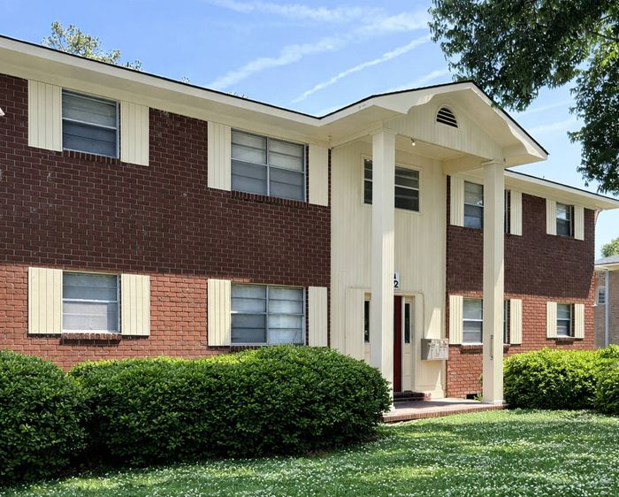 Charming two-story brick apartment building with inviting entryway and well-maintained green shrubs under a clear blue sky.