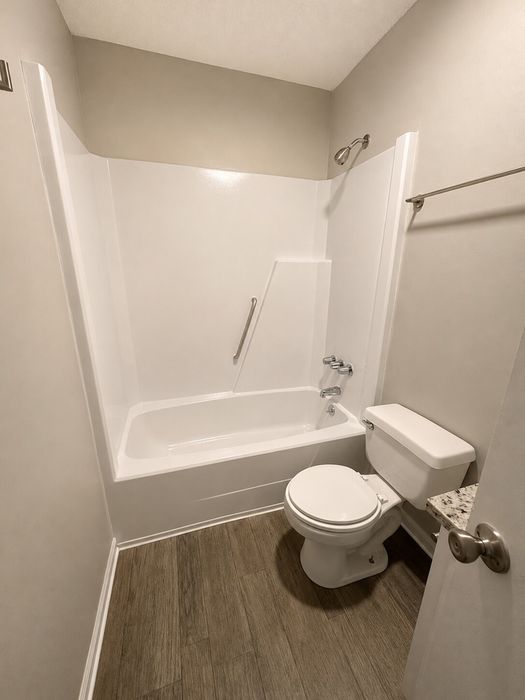 Modern bathroom featuring elegant wood-look flooring, sleek bathtub with safety bar, and pristine white fixtures.