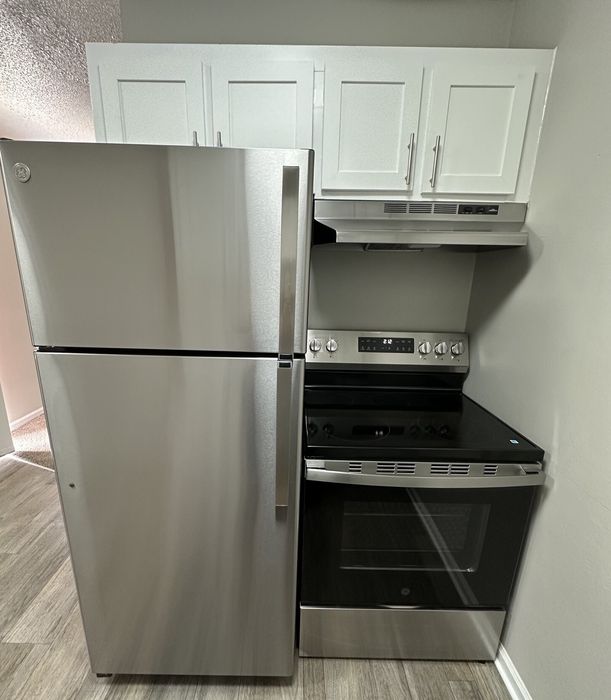 Modern kitchen with sleek stainless steel appliances, featuring a spacious fridge and an elegant stove against a backdrop of stylish white cabinetry.