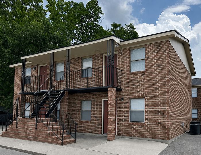 Charming two-story brick apartment building with modern iron railings and lush green surroundings.
