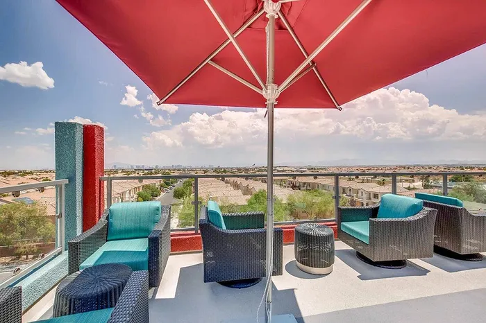 Inviting rooftop terrace featuring stylish wicker seating under a vibrant red umbrella, offering panoramic views of the surrounding neighborhood and distant mountains.