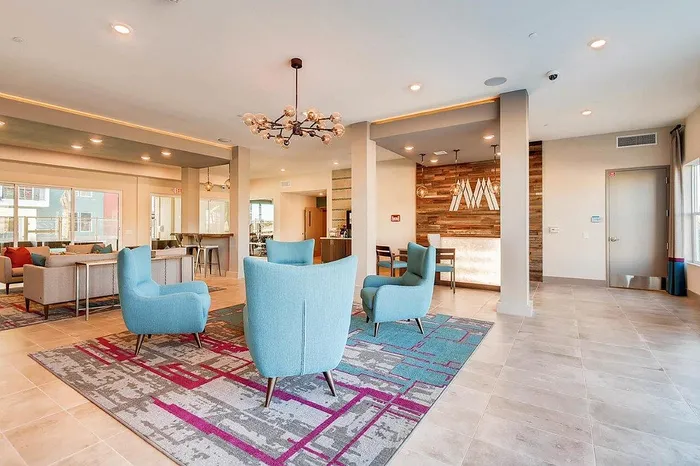 Modern apartment lobby with vibrant blue chairs, a chic chandelier, and a stylish reception area.