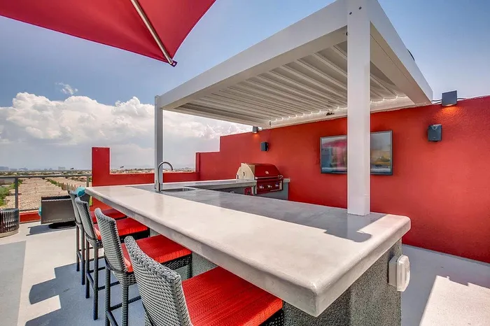 Luxurious rooftop patio featuring a sleek outdoor kitchen with a modern bar area, vibrant red accents, and panoramic views.