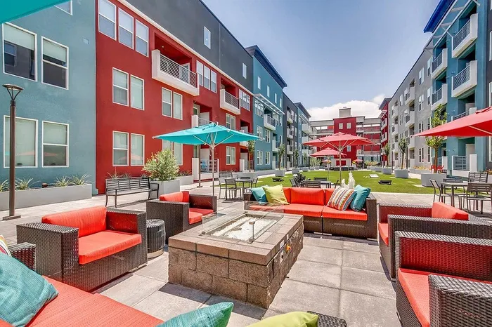 Vibrant apartment complex courtyard with colorful buildings, stylish outdoor seating, and lush landscaping under a clear blue sky.