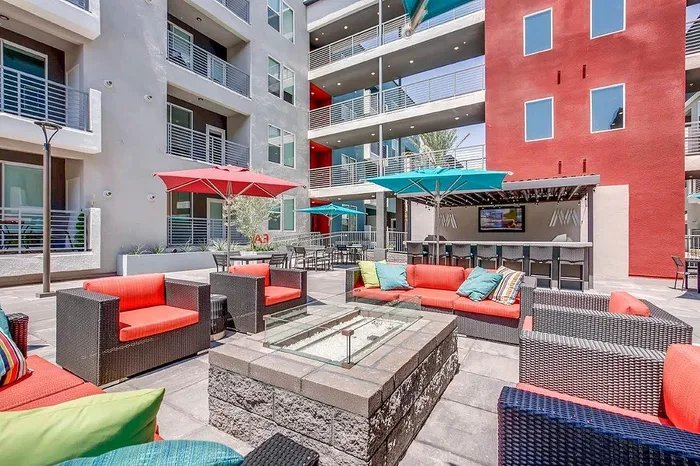 Modern apartment courtyard featuring vibrant red and turquoise furniture, stylish fire pit, and shaded lounge areas.