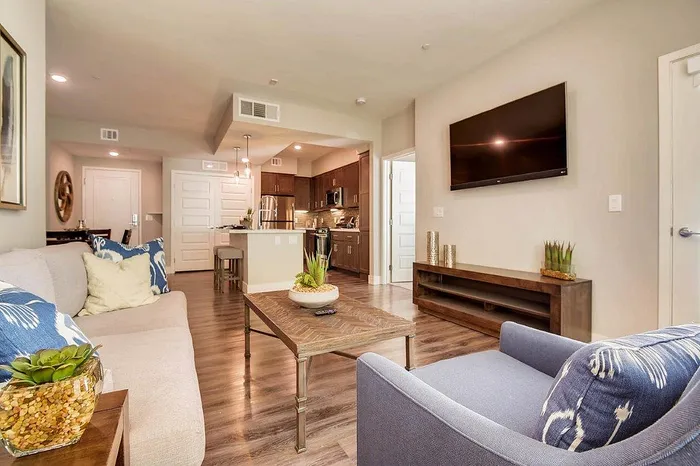 Modern open-plan living space with elegant furnishings, featuring a cozy sofa and vibrant decor, leading to a sleek kitchen with stainless steel appliances.