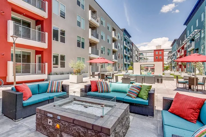 Modern outdoor courtyard featuring stylish seating, vibrant pillows, sophisticated fire pit, and colorful apartment facades.