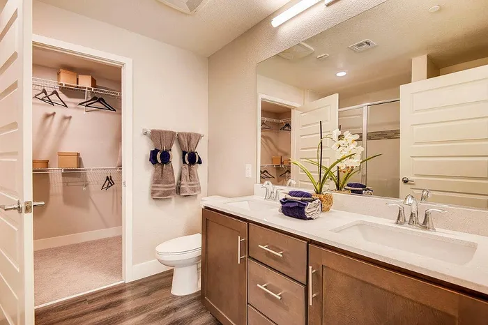 Elegant bathroom with dual sinks, modern cabinetry, and a spacious walk-in closet, enhanced by cozy towel decor and ambient lighting.