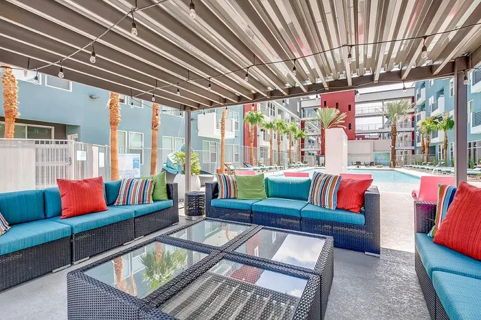 Modern outdoor lounge with colorful seating under a pergola, overlooking a sparkling pool at a stylish apartment complex.
