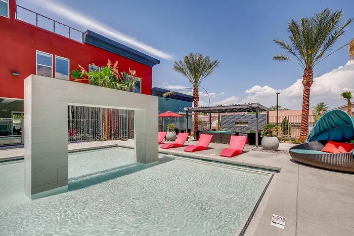 Luxurious outdoor oasis featuring a stunning pool with a waterfall feature, surrounded by modern red lounge chairs and lush palm trees.
