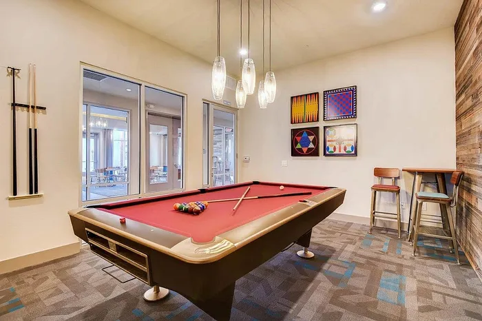 Chic recreation room with a vibrant red pool table, modern lighting, and stylish decor, complemented by tall stools and a cozy high table.