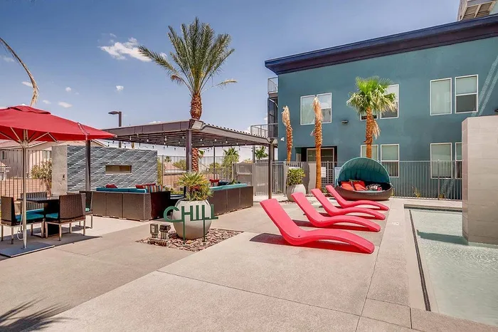Modern outdoor lounge with stylish red sun loungers, sleek cabana seating, and vibrant red umbrellas, offering a relaxing poolside retreat under clear blue skies.