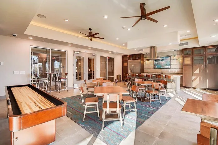 Bright and inviting communal lounge area with modern seating, a sleek shuffleboard table, and a stylish bar counter, perfect for social gatherings.