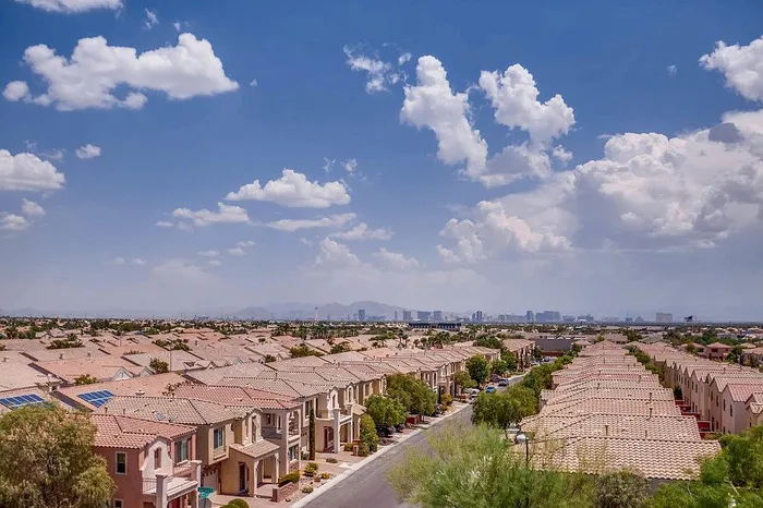 Charming suburban neighborhood with rows of stylish homes under a vibrant blue sky, offering a scenic view of distant city skyline.