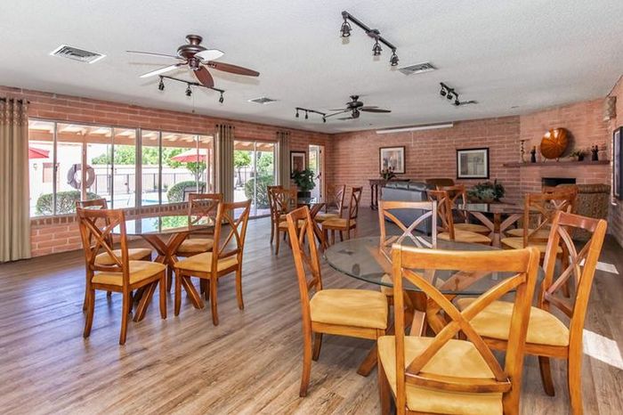 Inviting community room with stylish wooden chairs and glass tables, offering a view of the outdoor pool area through large windows.