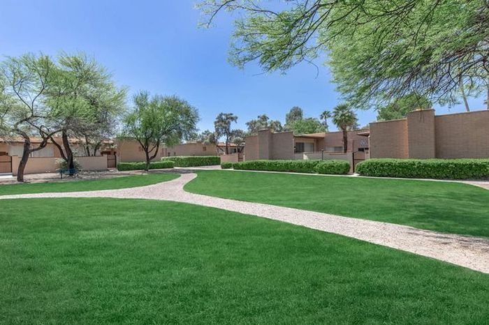 Beautiful community with lush green lawns, winding pathways, and well-maintained landscaping under a clear blue sky.
