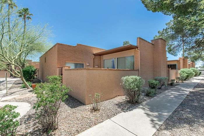 Charming single-story desert home with adobe-style architecture, lush landscaping, and a private patio under clear blue skies.