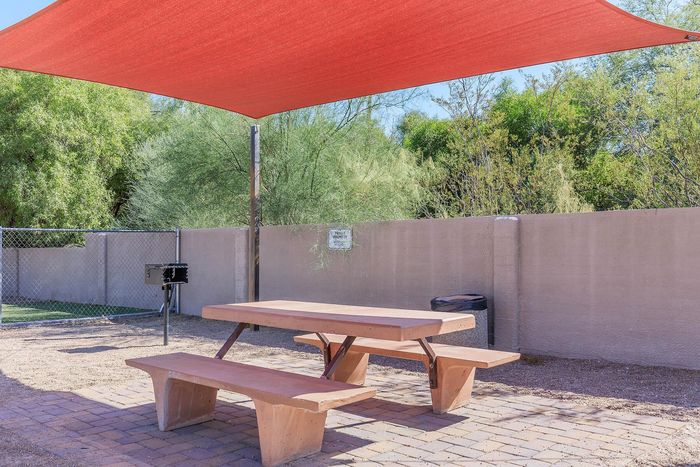 Inviting outdoor picnic area with a stylish shade canopy, perfect for grilling and entertaining amidst serene greenery.