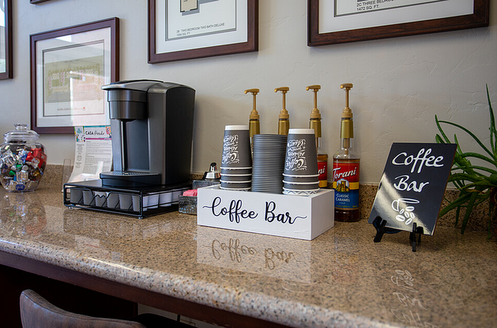 Inviting apartment coffee bar with modern espresso machine, decorative jars, and flavored syrups, perfect for residents to enjoy a warm beverage.