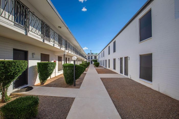 Inviting apartment complex with modern design, featuring white brick walls and well-maintained greenery lining the walkway on a clear, sunny day.