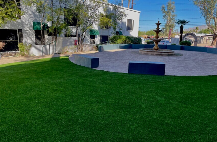 Tranquil outdoor courtyard with lush green lawn and elegant central fountain, surrounded by modern architecture.