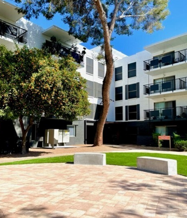 Elegant apartment building with modern balconies and lush courtyard, perfect for relaxing under the shade of mature trees.