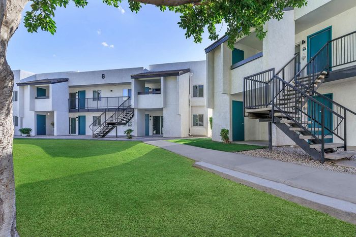 Modern apartment complex with lush green lawns, featuring stylish two-story buildings and sleek exterior staircases.