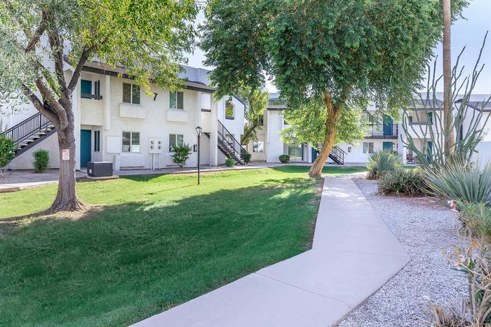 Charming apartment complex surrounded by lush greenery and a serene pathway, offering a peaceful residential environment.