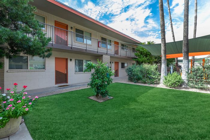 Charming two-story apartment building with lush green landscaping and vibrant flower beds, offering a peaceful and inviting living environment.