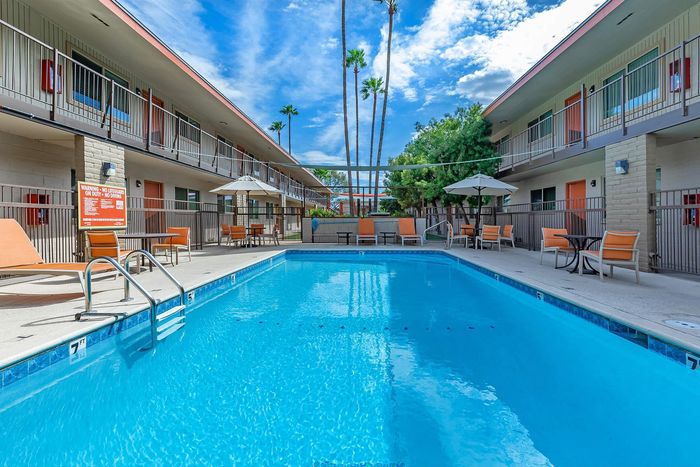 Inviting apartment courtyard featuring a sparkling blue pool surrounded by stylish orange lounge chairs and umbrellas, perfect for relaxing under sunny skies.